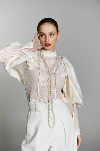 A young woman in a white lace blouse and pearl necklace poses against a grey background.