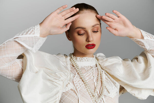 Woman in white lace blouse, pearl necklace, gazes downward, hands on forehead.