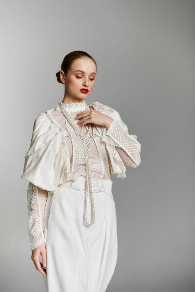 A woman in white attire stands against a gray background.