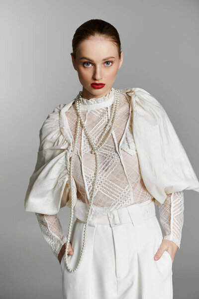 A young woman poses in a white lace top with pearl necklaces and a matching white pantsuit.