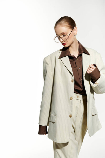 Девушка в красной помаде и очках в белом полосатом пиджаке и брюках в студии.