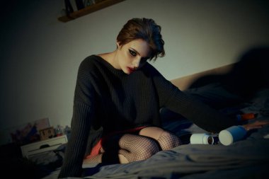 Donuk giyinmiş bir kadın loş bir odada yatağın üzerinde poz verir..