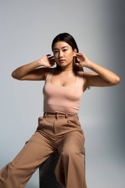 Pembe atletli ve kahverengi pantolonlu bir kadın kameraya doğru düşünceli bir şekilde oturur..