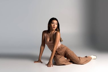 Şık giyinmiş genç bir kadın beyaz bir stüdyoda poz veriyor..