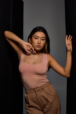 Şık giyimli bir kadın bir duvarın yanında durur, kollarını zarifçe uzatır..