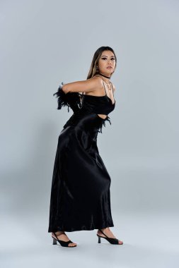 Siyah saten elbiseli bir kadın gri bir arkaplanda poz veriyor..