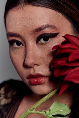 A close-up portrait of an Asian woman with a red flower partially covering her face. clipart