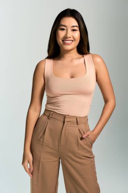 A woman with long black hair and a bright smile is wearing a pink tank top and brown slacks. clipart