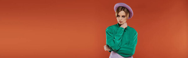 A woman wearing a green shirt and a purple beret poses against a bright orange background.