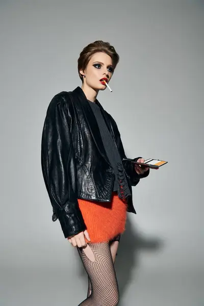 stock image A stylish woman in a black leather jacket and orange fuzzy skirt poses confidently with a cigarette.