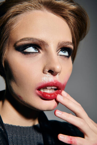 Женщина с грязным, темным макияжем и красной помадой смотрит вверх, ее палец отслеживает ее губы.