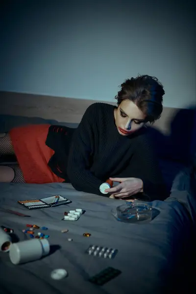 stock image A woman in stylish attire poses on a bed, surrounded by scattered pills and pill bottles.