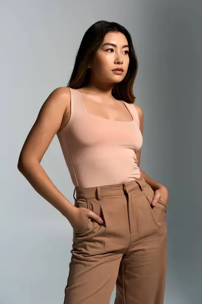 stock image Woman in fashionable tank top and trousers gazes beyond camera against gray backdrop.