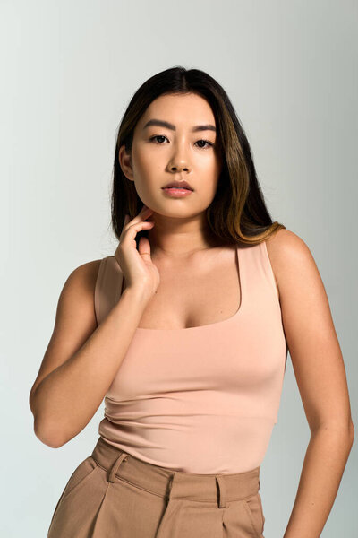 Молодая женщина с длинными темными волосами позирует с уверенным выражением лица во время ношения персикового топа.