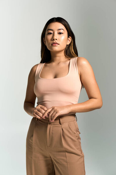 Красивая азиатка в розовом топе и коричневых брюках уверенно позирует.