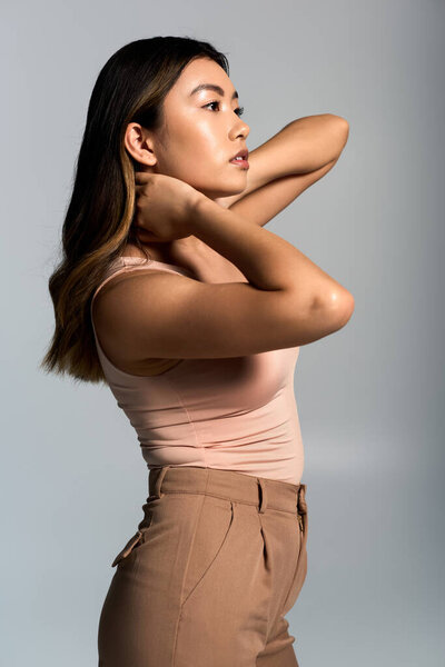 Молодая женщина, одетая в розовый топ и коричневые брюки, смотрит вдаль.