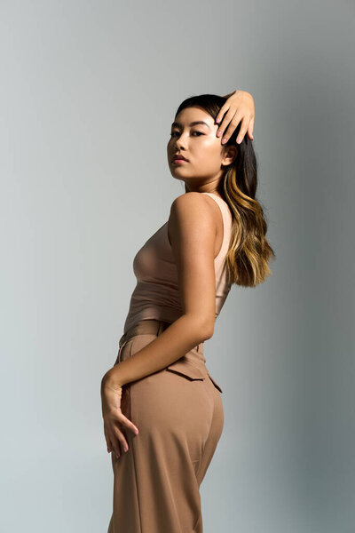 A woman in a stylish tan top and pants poses confidently in a studio setting.