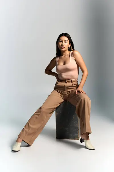 stock image An Asian woman in a light pink top and wide-legged brown pants poses on a concrete block.