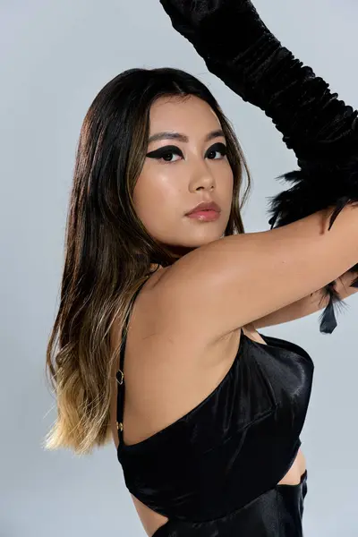 stock image A young woman wearing a black satin dress and feather gloves poses in front of a plain background.