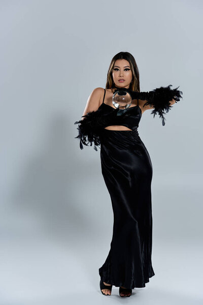 A woman in a black dress and feather gloves holds a crystal ball.