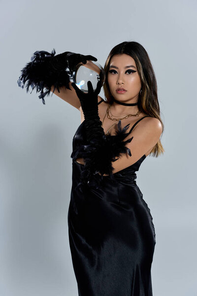 Женщина в черном платье и перчатках пристально смотрит в хрустальный шар.