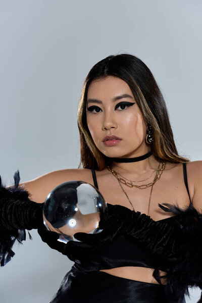 Женщина в черном держит хрустальный шар, глядя в неизвестность.