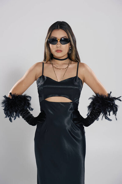 Woman in black dress and feather gloves gazes intensely in studio.