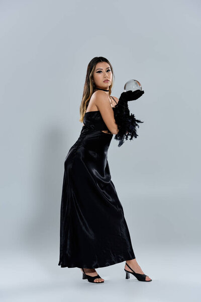 A woman in a sleek black gown and gloves holds a crystal ball, her gaze fixed on its secrets.