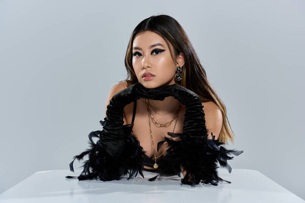 Азиатка в черных перчатках опирается на белую поверхность, смотрит в камеру.
