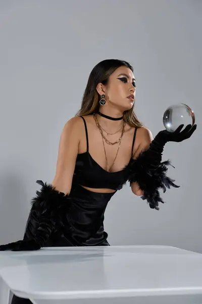 stock image A woman in a black dress and gloves holds a crystal ball, gazing intently at its reflections.