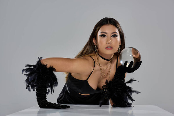 Женщина в черном наряде пристально смотрит в хрустальный шар.