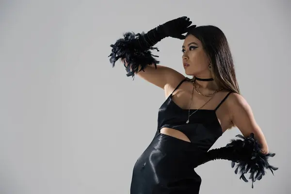 stock image A captivating woman in a stylish black dress and feather gloves poses against a minimalist backdrop.