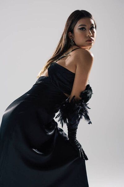 Женщина в черном атласном платье позирует с боа пера.