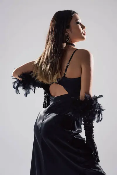 stock image A woman in a black satin dress with feathered gloves looks over her shoulder.