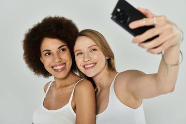Kolsuz tişört giyen iki kadın selfie için poz veriyor..