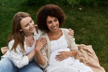 A pregnant woman, cradling her belly, smiles lovingly as her partner rests a hand on her shoulder. clipart