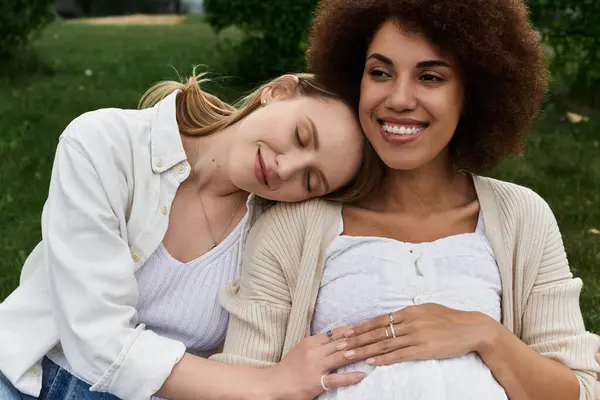 stock image A pregnant woman rests her head on her partners shoulder as they enjoy a peaceful moment in a park.
