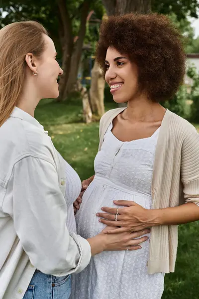 stock image A pregnant Black woman wearing a white dress, smiles lovingly as her partner holds her belly.