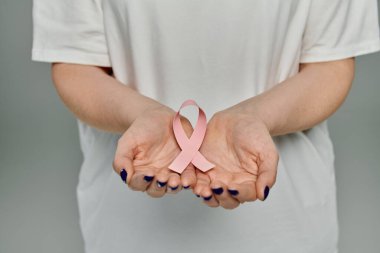 Bir kadın, kavrulmuş ellerinde pembe bir kurdele tutuyor. Bu da meme kanseri farkındalığını gösteriyor..
