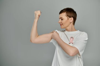 A woman with short hair flexes her bicep, displaying a pink ribbon symbolizing breast cancer awareness. clipart