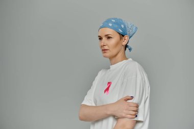 Kısa saçlı bir kadın mavi bir bandana ve pembe kurdeleli beyaz bir gömlek giyiyor..