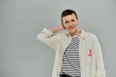 A woman with short hair smiles confidently, wearing a pink ribbon on her shirt, symbolizing breast cancer awareness. clipart