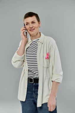 Gömleğine pembe kurdele takmış bir kadın cep telefonuyla konuşuyor..
