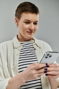 Kısa saçlı ve günlük kıyafetli bir kadın akıllı telefon kullanırken gülümsüyor..