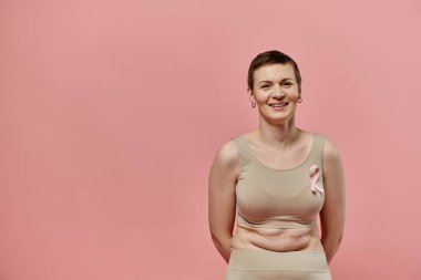 A woman with short hair smiles confidently, wearing a pink ribbon in support of breast cancer awareness. clipart