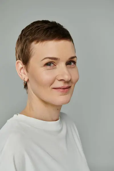 stock image A woman with short brown hair smiles, wearing a white shirt, with a hopeful expression.