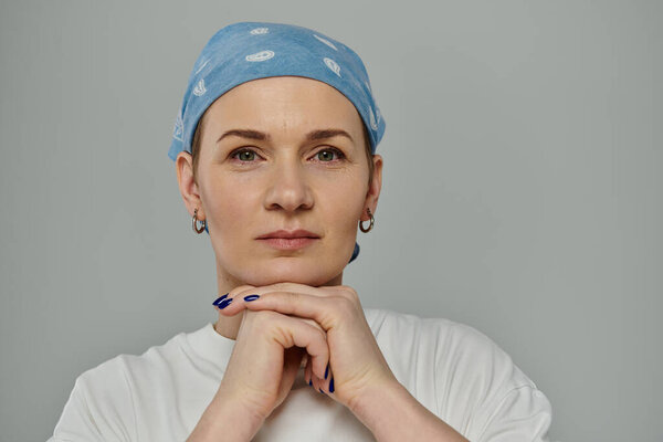 A woman with short hair, wearing a blue bandana and white t-shirt, looks directly at the camera with a serious expression.