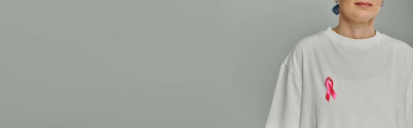 Женщина с короткими волосами носит белую футболку с розовой лентой на ней, символ осознания рака груди.