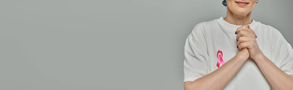 Женщина с короткими волосами носит розовую ленту в поддержку информированности о раке молочной железы, ее руки сжимаются в молитве.