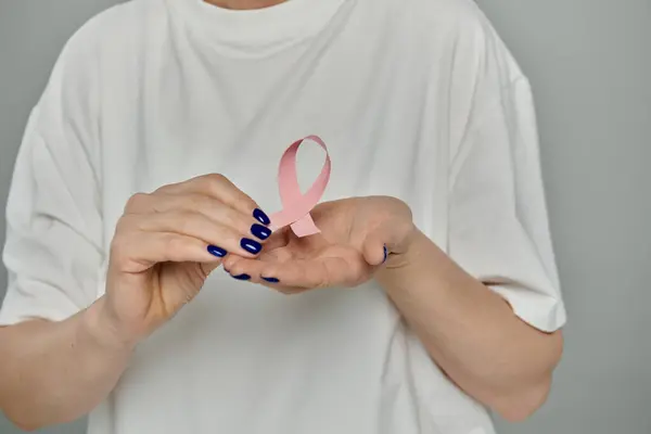 stock image A woman holds a pink ribbon in her palm against a grey background.